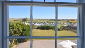 Blick durch ein Fenster auf eine ländliche Landschaft mit Häusern, Grünflächen und blauem Himmel.