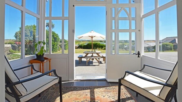 Ein Wintergarten mit zwei Stühlen, einem Tisch und Blick auf eine Terrasse mit Picknicktisch und Sonnenschirm.