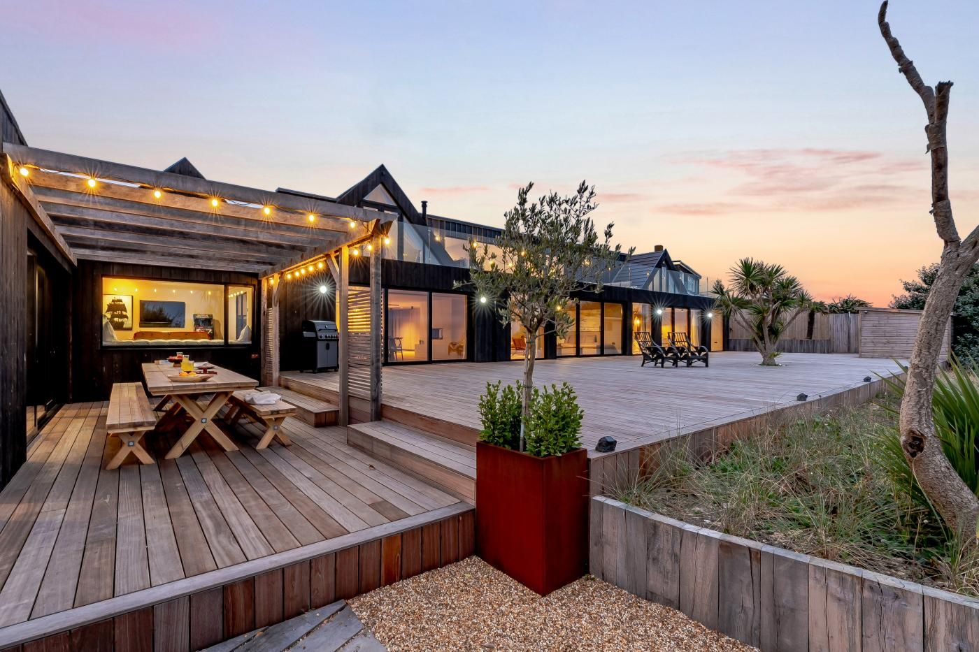A modern outdoor patio area with a wooden deck, a barbecue grill, and a seating arrangement.