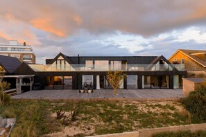 A modern house with a deck, large windows, and a view of the beach.
