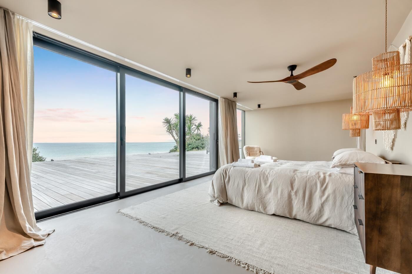 A bedroom with a large sliding glass door leading to a wooden deck overlooking the sea.