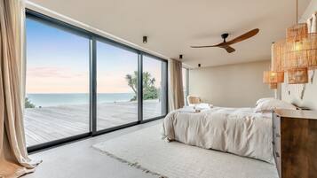 A bedroom with a large sliding glass door leading to a wooden deck overlooking the sea.