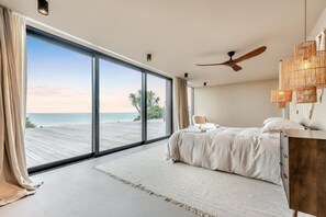 A bedroom with a large sliding glass door leading to a wooden deck overlooking the sea.