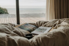 A bed with a book and a cup, a window with a view of the beach, and curtains. - 5 Bed in Bexhill-on-Sea (oc-c32704) (Bexhill-on-Sea)
