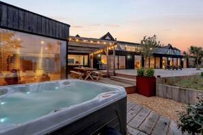 A modern outdoor patio with a hot tub, wooden deck, and string lights.