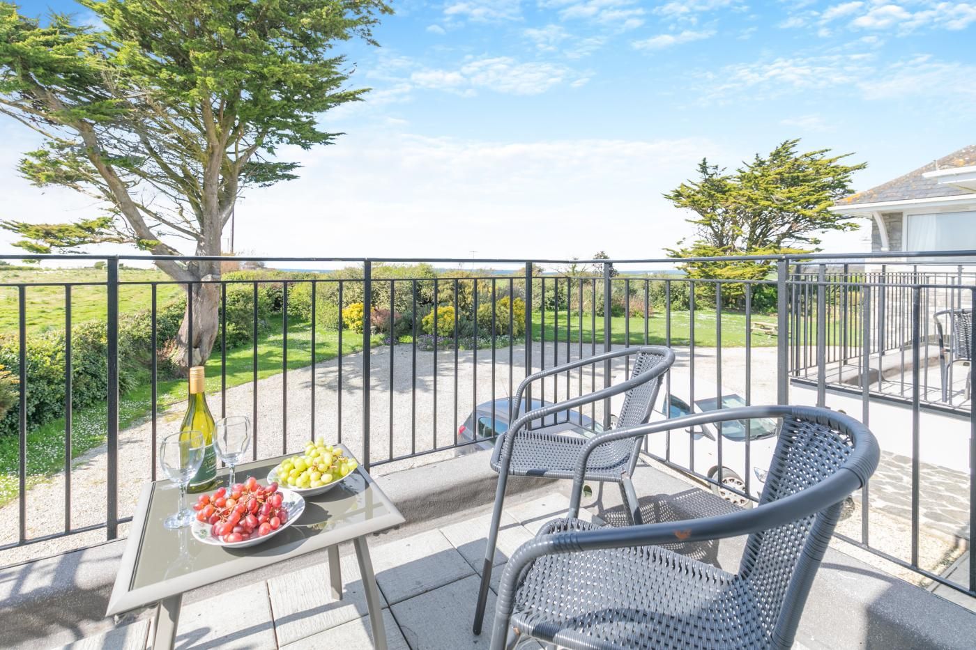 An outdoor patio with a table set for two, featuring a bottle of wine, a bowl of grapes, and a plate of tomatoes.