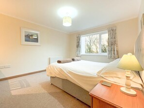 Une chambre à coucher avec un lit, une table de chevet avec une lampe, une fenêtre avec des rideaux, un radiateur et un tableau encadré au mur.