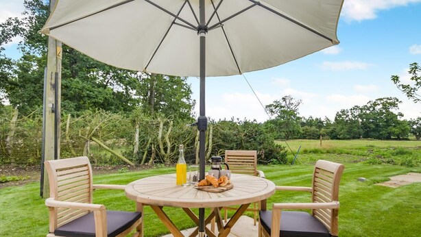 A round wooden table with two chairs, an umbrella, and a bottle of orange juice. - 1 Bed in Wymondham (oc-e32664) (Wymondham)