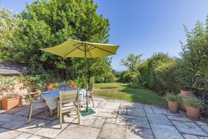 An outdoor patio with a table and chairs, a yellow umbrella, and potted plants.