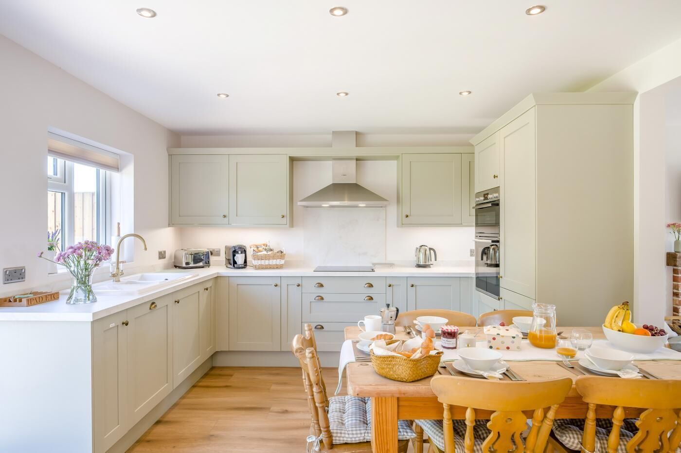 Een keuken met een eethoek, met lichte kastjes, een houten eettafel en een raam dat voor natuurlijk licht zorgt.