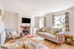 Ein gemütliches Wohnzimmer mit Kamin, einer Couch, einem Fernseher und einem Fenster mit Vorhängen.