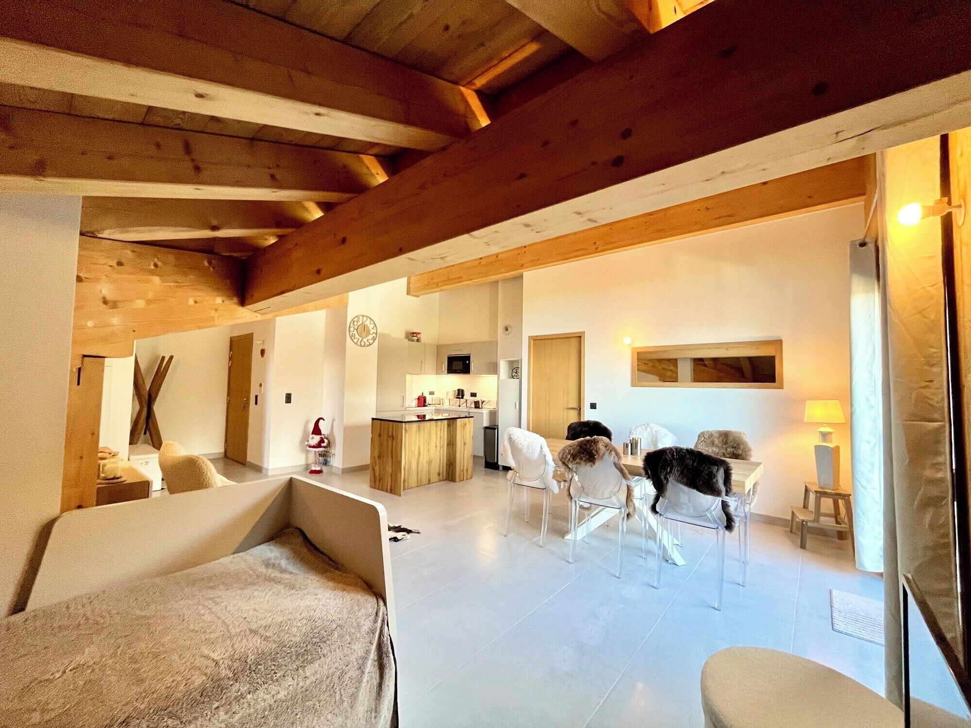Un'ampia zona giorno con soffitto alto e travi in legno, una cucina sullo sfondo e un'area pranzo con sedie e tavolo.