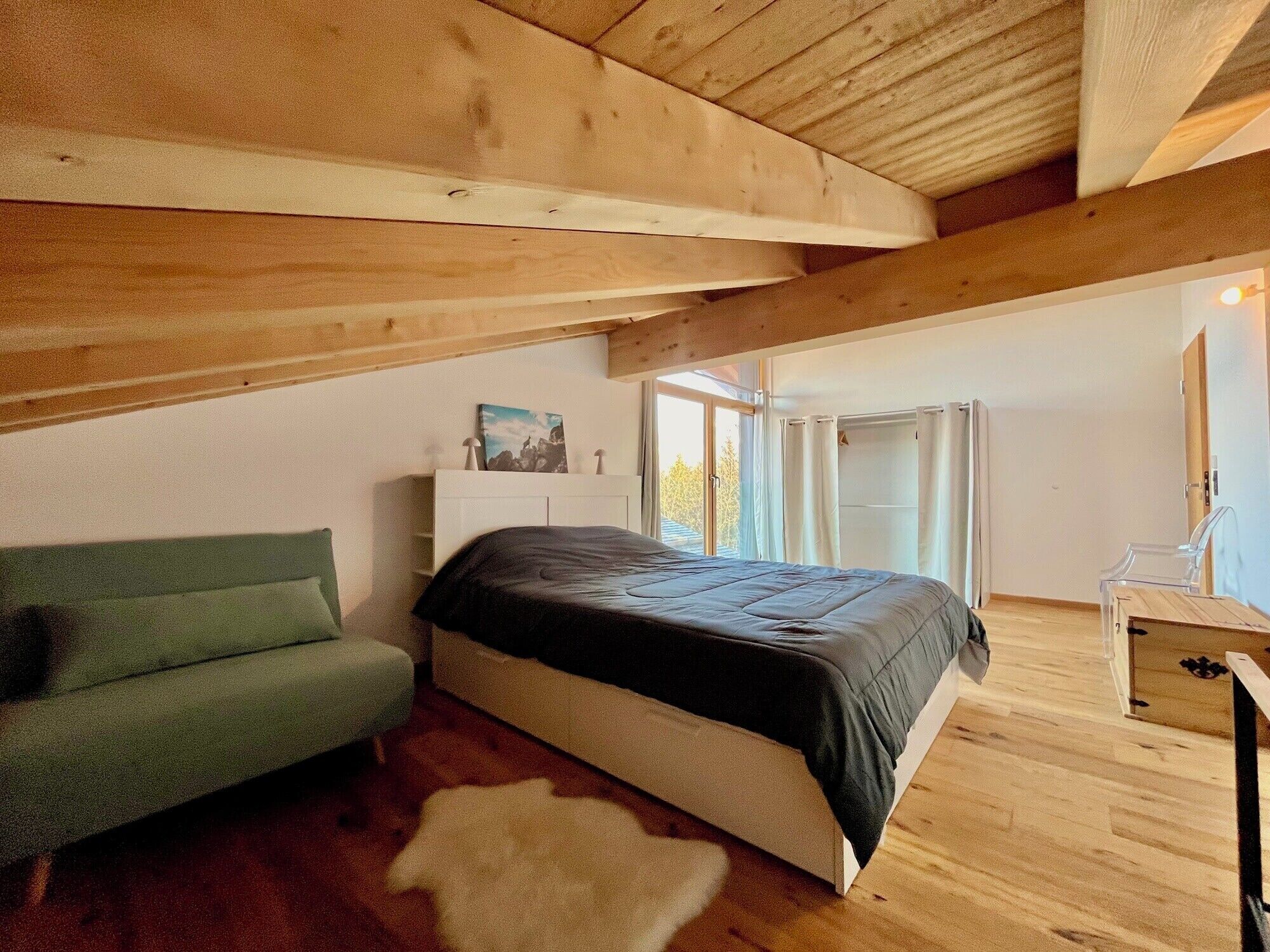 Ein Schlafzimmer mit einem Bett, einem grünen Sofa, einer Holzbalkendecke und einem Fenster.