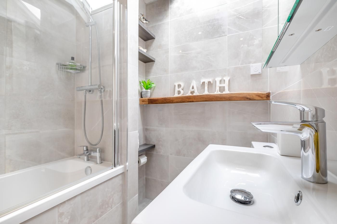 Een moderne badkamer met een douchecabine van glas, een witte wasbak en een plank met de tekst 'BATH' op de muur.
