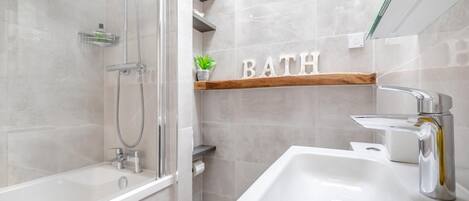 A modern bathroom with a glass-enclosed shower, a white sink, and a shelf with the word 'BATH' on the wall.