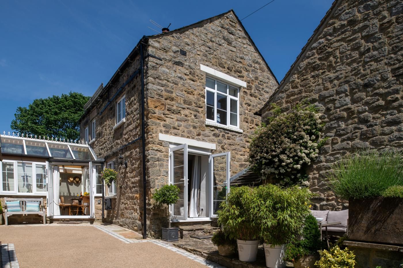 A stone building with a large open door, a window, and a small garden area with potted plants.