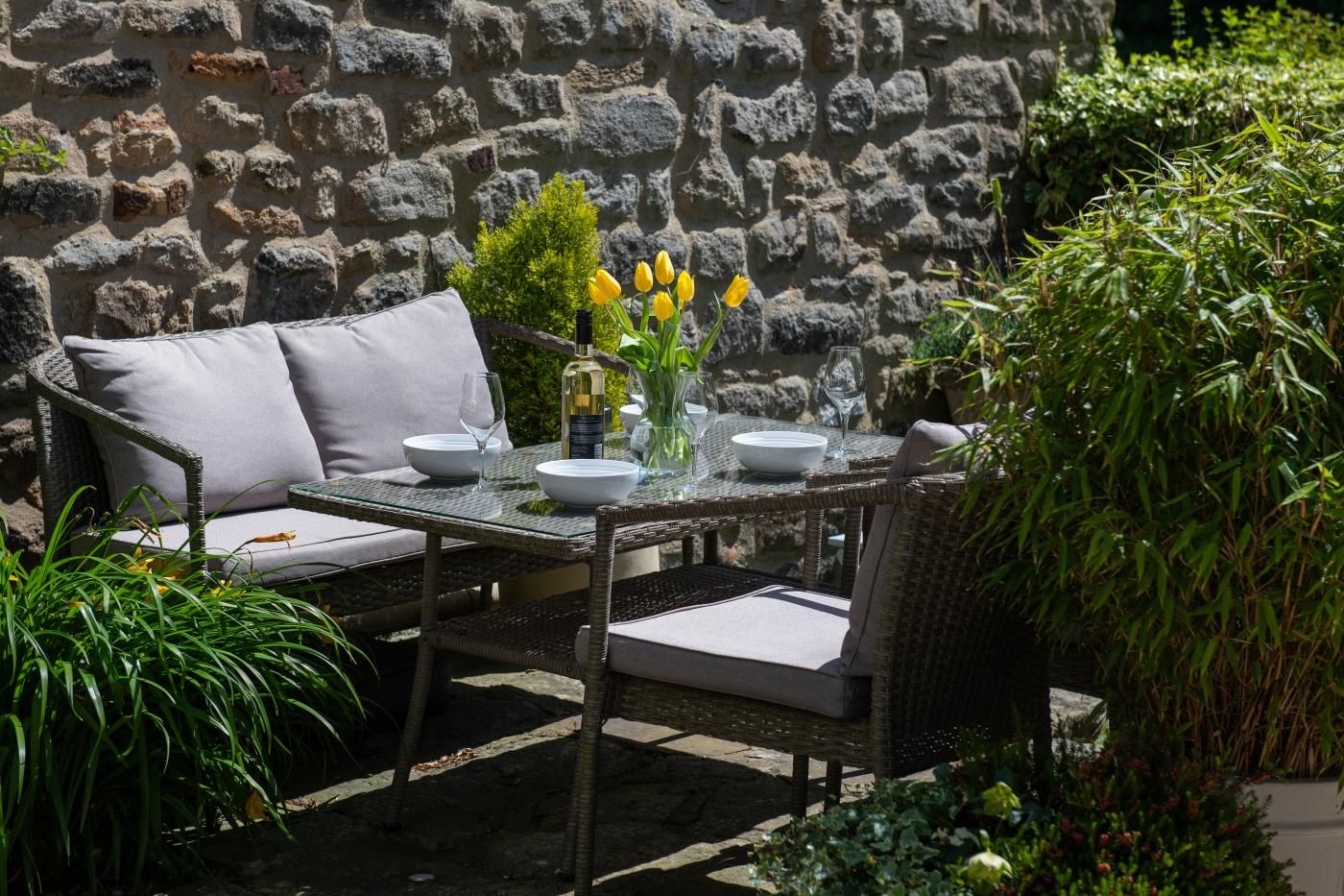 An outdoor dining area with wicker furniture and a stone wall backdrop.