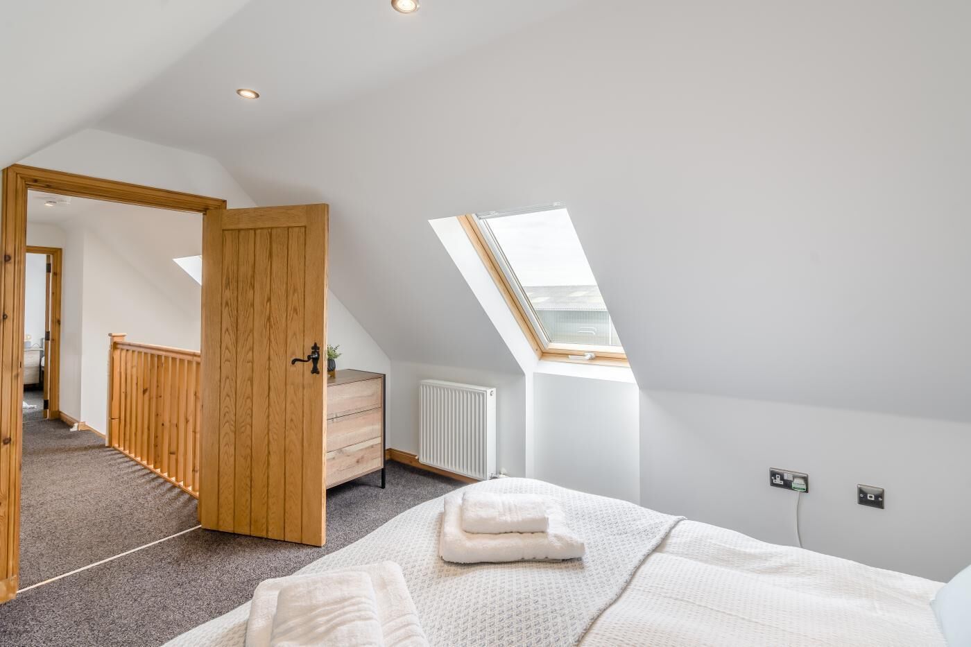 Un dormitorio moderno con techo inclinado, tragaluces, armario de madera, radiador y cama bien hecha.