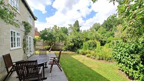 A patio with a table and chairs, surrounded by a well-maintained lawn and various plants.