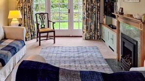 A cozy living room with a fireplace, a sofa, a chair, and a large window with curtains.