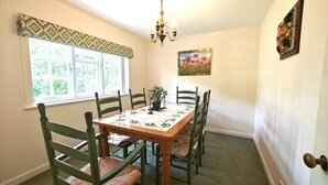 A dining room with a wooden table and six chairs, a chandelier, a window with patterned curtains, and a painting on the wall.
