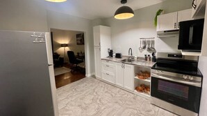 A modern kitchen with white cabinets, a stainless steel oven, and a black microwave. There are two pendant lights and a sink with a faucet. - Downtown Retreat Moncton (Moncton)