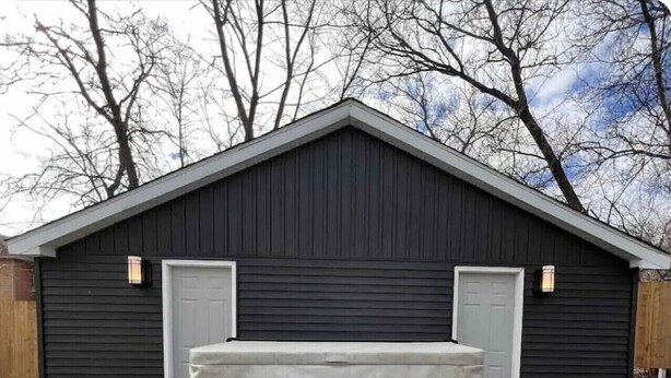 A wooden deck with a hot tub in front of a black building with two doors. - Downtown Retreat Moncton (Moncton)