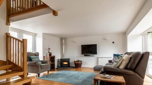 Un salon spacieux avec un escalier en bois, une cheminée, un canapé, un téléviseur et une grande fenêtre.