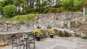 Une terrasse extérieure avec un sol en pierre, deux chaises en métal, une table ronde et des plantes en pot.