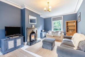A living room with a fireplace, sofa, ottoman, TV, and a wooden cabinet. - 4 Bed in Matlock Bath (oc-r32432) (Matlock Bath)