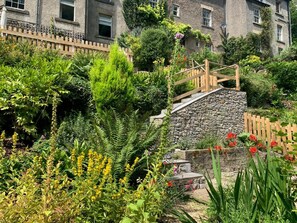 A stone staircase leading up to a wooden deck, surrounded by lush greenery and flowering plants. - 4 Bed in Matlock Bath (oc-r32432) (Matlock Bath)