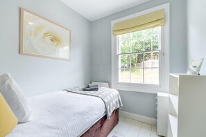 Ein Schlafzimmer mit einem Bett, einem Fenster mit Blick auf Grünflächen, einem Heizkörper und einem Nachttisch.