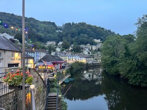 Eine Stadt am Flussufer mit Gebäuden entlang des Wassers, einer Brücke und einer Treppe, die zum Fluss hinabführt.