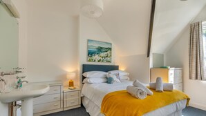 A hotel room with a bed, a bedside table with a lamp, a sink, and a painting on the wall. - 3 Bed in Beer (oc-mbcvw) (Beer)
