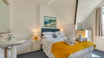 A hotel room with a bed, a bedside table with a lamp, a sink, and a painting on the wall.