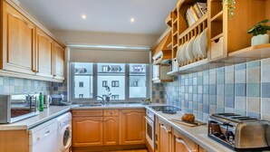 A modern kitchen with wooden cabinets, a built-in oven, a sink, and a window with a view of buildings. - 3 Bed in Beer (oc-mbcvw) (Beer)