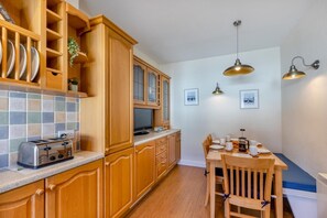 Une cuisine avec des meubles de rangement en bois, un grille-pain, une table à manger avec des chaises et des luminaires suspendus.