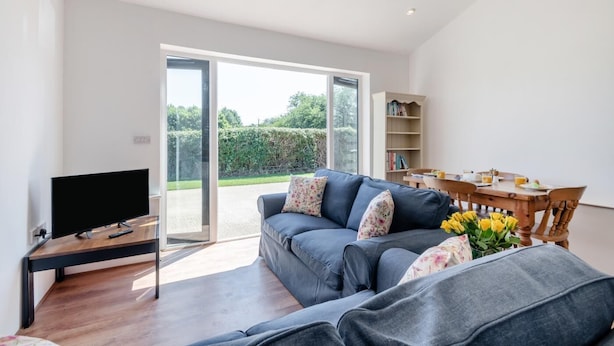 A modern living room with a grey sofa, a flat-screen TV, a wooden coffee table, and a dining table with chairs. - 2 Bed in Fressingfield (oc-j32677) (Fressingfield)