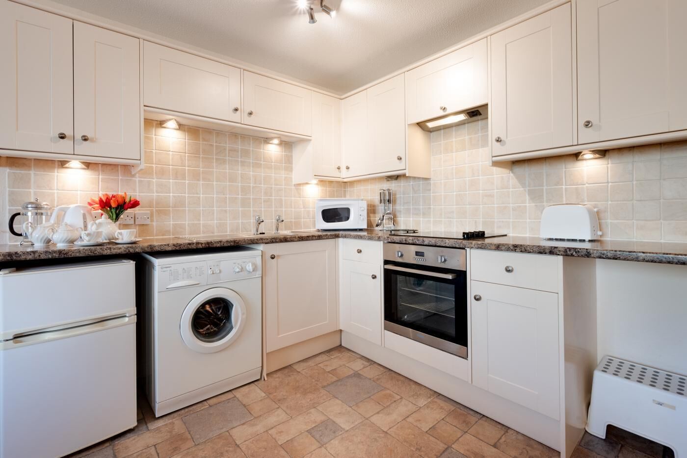 A modern kitchen with white cabinetry, a built-in oven, a microwave, a washing machine, and a toaster.