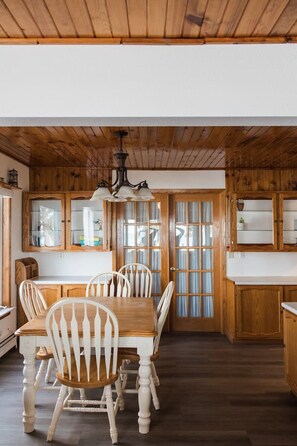 Un comedor con mesa y sillas de madera, una araña y armarios de madera.