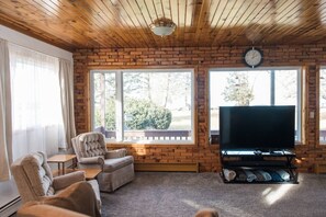 Un salón acogedor con pared de ladrillo, ventanas amplias, un televisor de pantalla plana y asientos cómodos.