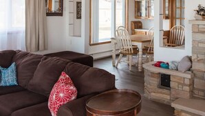 Een gezellige woonkamer met een bruine bank, een ronde houten tafel en een stenen openhaard.