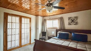 Een slaapkamer met een houten plafond, een bed met blauw-witte beddengoed, een bureau met een stoel en een raam met gordijnen.