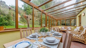 Une véranda avec une table à manger pour quatre personnes, entourée de meubles en osier et offrant une vue sur le jardin.