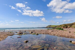 Une plage rocheuse avec une eau claire et, en arrière-plan, une colline couverte d’herbe.