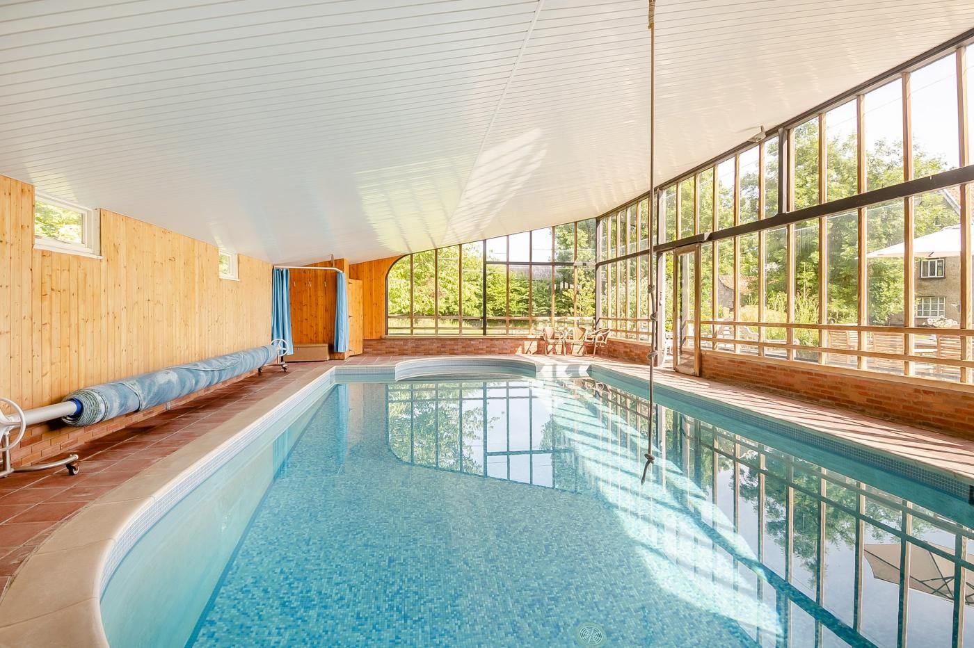 Une piscine intérieure avec un revêtement en bois, de grandes fenêtres et une vue dégagée sur l’extérieur.