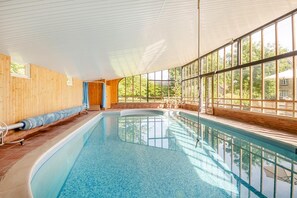 En inomhuspool med träpanel på väggarna, stora fönster och fri utsikt över omgivningen.