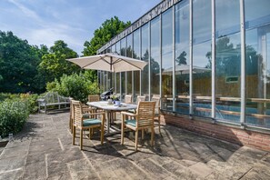 Una veranda esterna con tavolo e sedie, un barbecue e un'ampia struttura in vetro.
