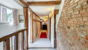 A hallway with exposed wooden beams, brick walls, and a red carpet.