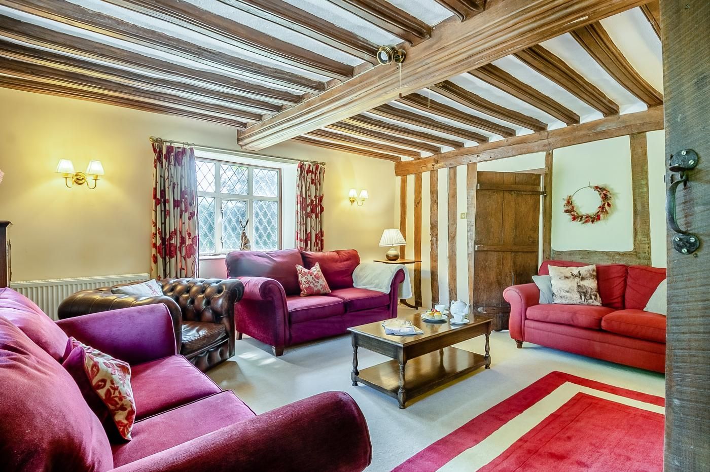 A cozy living room with a fireplace, wooden beams, and a large window with curtains.